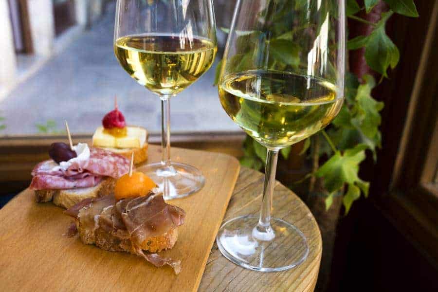 Different kind of the Cicchetti - italian tapas, small snacks with prosciutto, brie cheese, seafood, meat and other stuffing with two wine glasses of white wine