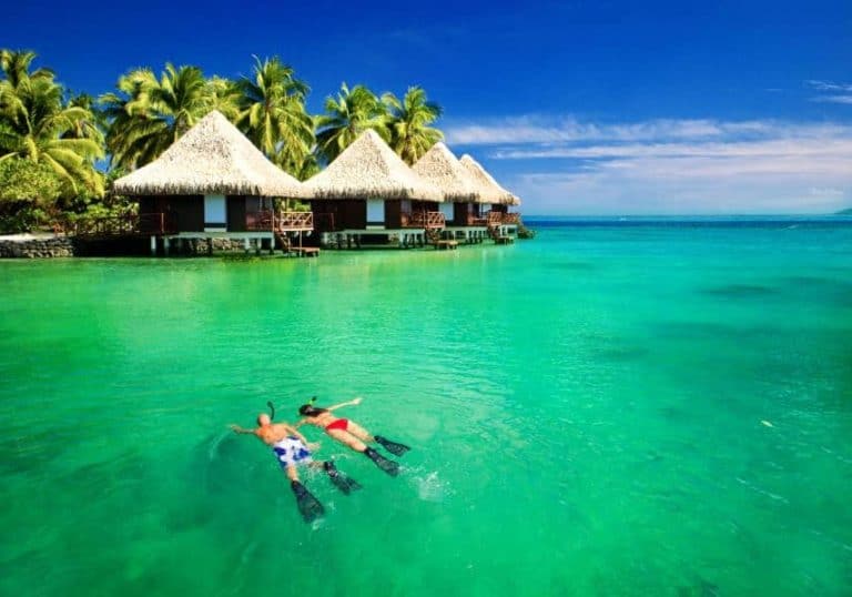 Couple snorkling in tropical lagoon with over water bungalows